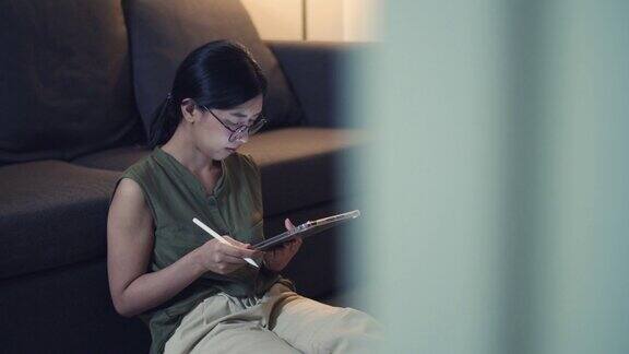一名亚洲女性晚上坐在客厅的沙发上用她的数码平板电脑看新闻