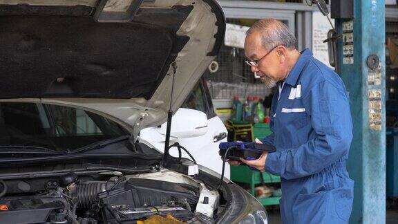 亚洲资深汽车技工在车库检查和使用技术修理老亚洲汽车修理工工作
