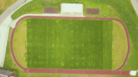 农村学校建筑附近的体育场鸟瞰图红色的跑道和绿色的草地足球场