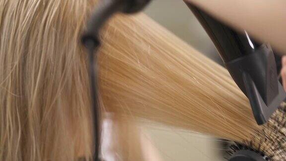 干燥的金发的特写手用圆刷把一缕发丝用吹风机吹几次直至发丝变长
