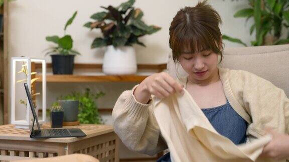 年轻的亚洲妇女从纸箱中打开新购买的衣服从她的网上购物零售送货上门