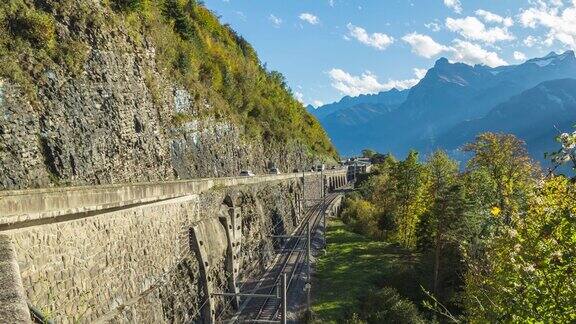 随着时间的推移汽车和火车在裸露的岩石山旁边的道路上通行施维茨州莫沙赫