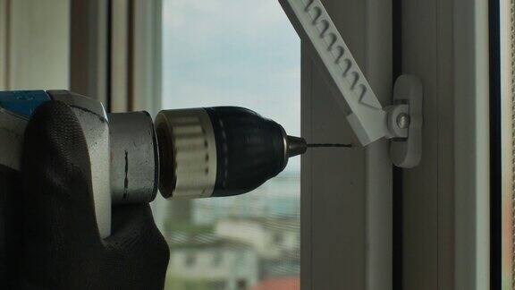 男用电钻在塑料窗框上钻孔安装窗塞用于安装窗口限制器、特写的紧固件钻孔用电钻钻孔回家修理