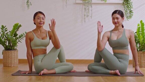 一对亚洲年轻女子坐在瑜伽垫上做呼吸练习瑜伽伸展肌肉一起热身两位健康女性的瑜伽冥想平衡身体在舒适的家中放松