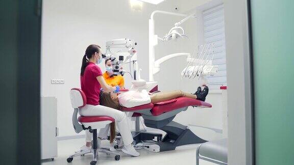 在现代牙科诊所女牙医带着助手用显微镜治疗牙齿特写视图