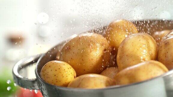 在明亮的厨房里未剥皮的土豆在水滴下用滤器冲洗