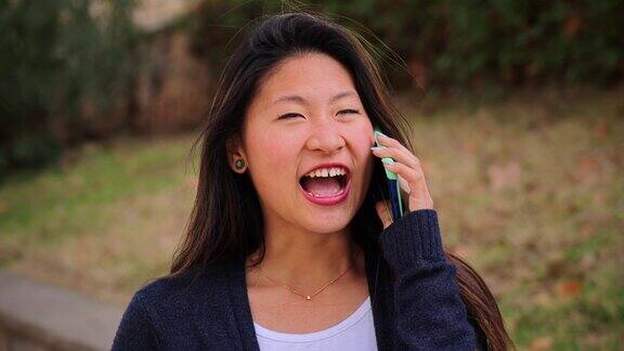 快乐的十几岁的女学生微笑着用手机交谈快乐、无忧无虑的年轻中国女人在外面用智能手机聊天亚洲八卦女用手机交流
