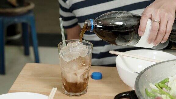 4kCloseUp男人的手拿着一个可乐瓶倒入一个装满冰的透明玻璃杯准备它