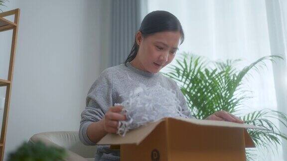 一名亚洲妇女坐在家里的客厅里打开网上购物的纸箱打开包装检查商品