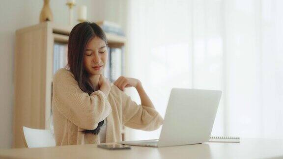 办公室综合症年轻的亚洲女性在长时间使用笔记本电脑后感到脖子和肩膀疼痛她伸伸懒腰放松肌肉
