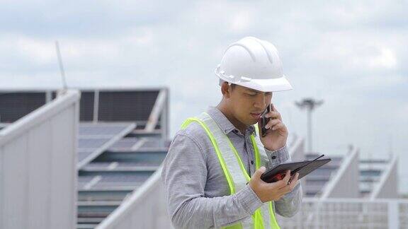 电气工程师在屋顶上检查太阳能电池板的构造并使用智能手机和数码平板电脑