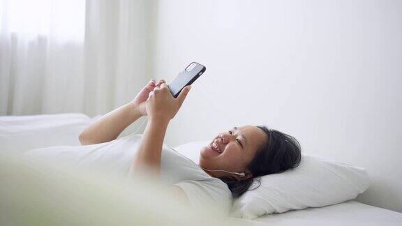 年轻女子戴着耳机躺在床上白天喜欢用手机