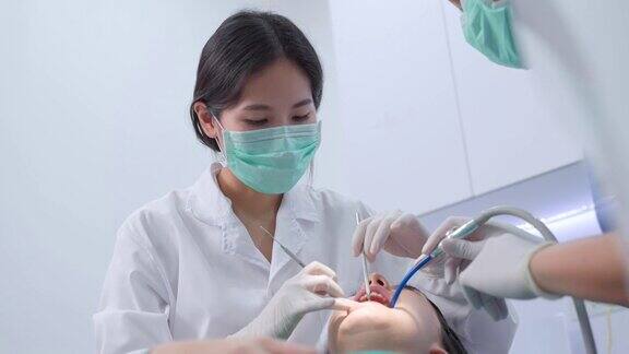 亚洲年青牙医戴上口罩使用医疗器械进行口腔护理治疗助手坐在旁边使用吸痰机牙科诊所的医疗服务职业和保健