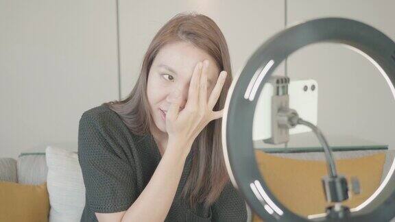 美丽的东南亚女性博主正在展示如何化妆和使用化妆品在摄像机前录制vlog视频直播在家在社交媒体和副业概念上的商业在线影响者
