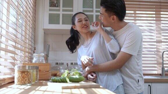 年轻漂亮的亚洲夫妇在家里的厨房里做健康的食物边说边笑