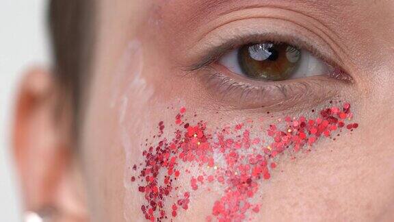 化妆刷在棕色眼睛的女模特脸上涂上红色闪光的特写镜头