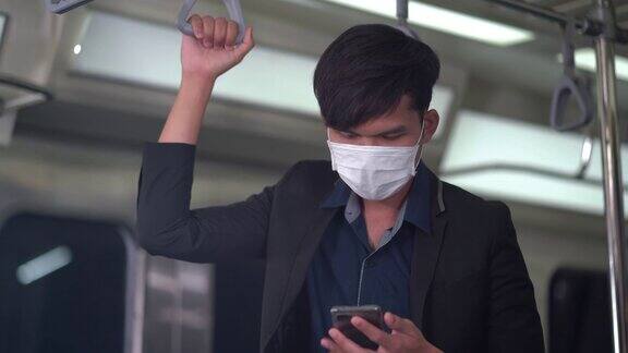 亚洲年轻商人戴着医用口罩在地铁里用智能手机预防感染冠状病毒在Covid-19大流行期间公共交通处于新常态的乘客