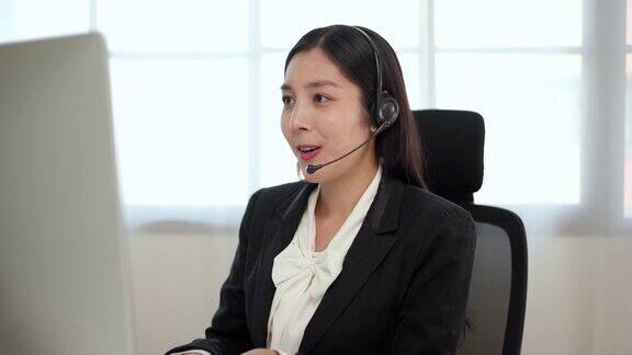 Smiley亚洲商务女接待员戴耳机视频会议电话在电脑上通过网络摄像头在网上聊天客户支持服务