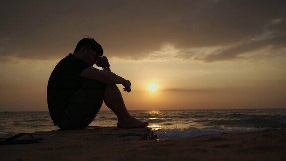 亚洲男子沮丧和坐在海滩日落芭堤雅