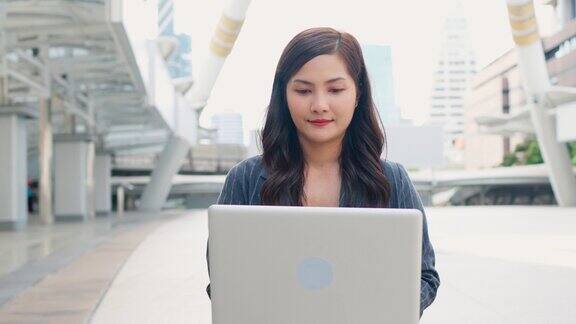 微笑的亚洲商务女性在商务区办公室外使用笔记本电脑处理紧急工作科技无处不在