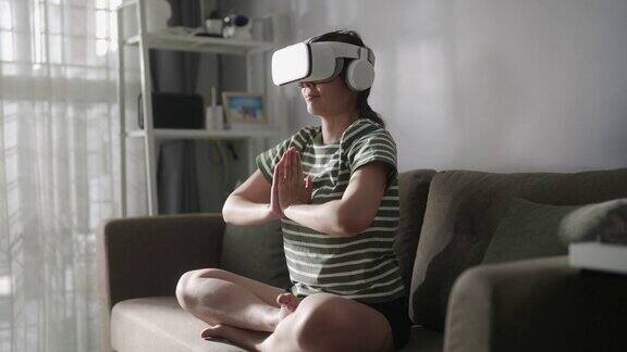 戴着虚拟现实眼镜的女性正在家中冥想双手合十享受模拟和放松
