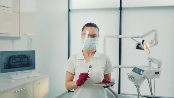 在医务室戴口罩的女牙医从托盘中取出口内镜在挑选牙科工具的手套中漂亮助手的肖像视图在室内看着相机牙科