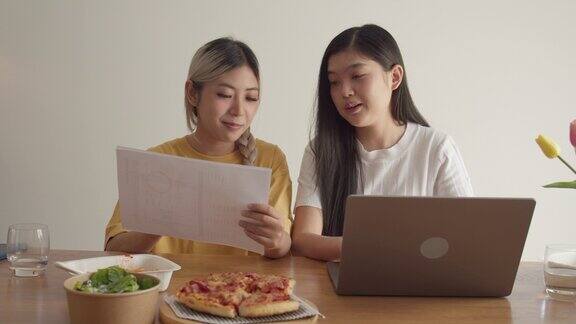 一个亚洲女人一边吃披萨一边在家里用笔记本电脑工作