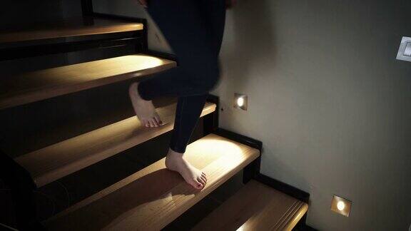 中镜头的女性赤脚青少年走下楼梯在晚上用奢华的led灯点亮