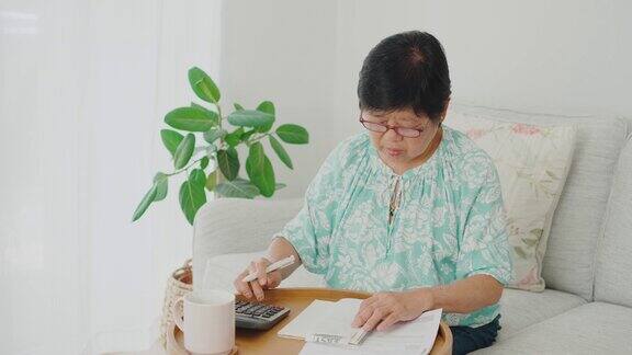 亚洲老年妇女在客厅整理支付账单和家庭财务通货膨胀和金融危机