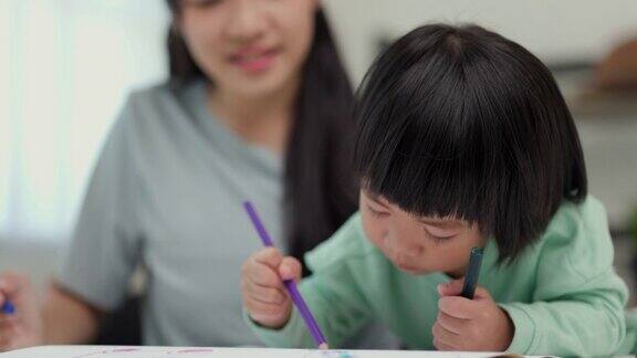 快乐的亚洲男孩与他的母亲在客厅里用蜡笔和彩色铅笔画画妈妈教儿子如何用蜡笔在书上画画或做作业家庭