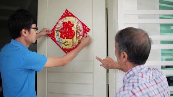 亚洲华人的儿子和父亲在中国新年前夕用“财运”春联装饰他的房子