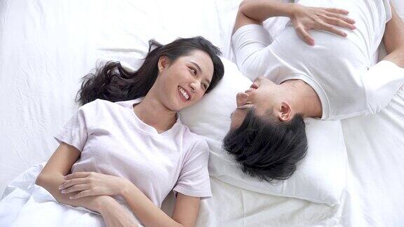 快乐的亚洲情侣躺在床上微笑一起放松