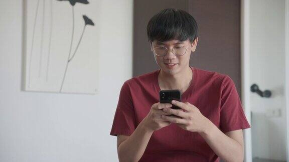 亚洲男子戴着眼镜坐在沙发上的早上他的手机收到短信非常高兴和微笑4k决议