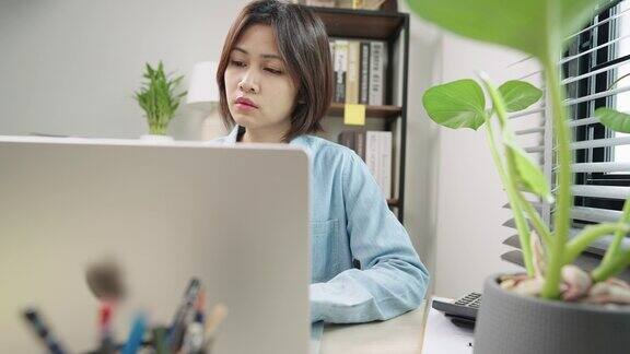年轻的亚洲女商人在家里、办公室或公寓用笔记本电脑上网研究