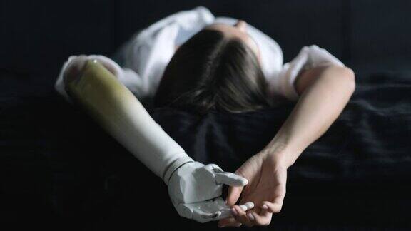 用仿生手臂合上女子的两只手人失去了手臂女孩的人工假肢躺在黑色的床上