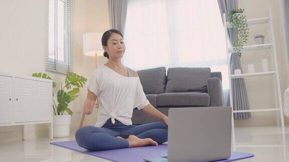 美丽快乐的年轻亚洲妇女热身在线瑜伽课在她的客厅在周末在家在线学习健康的生活方式