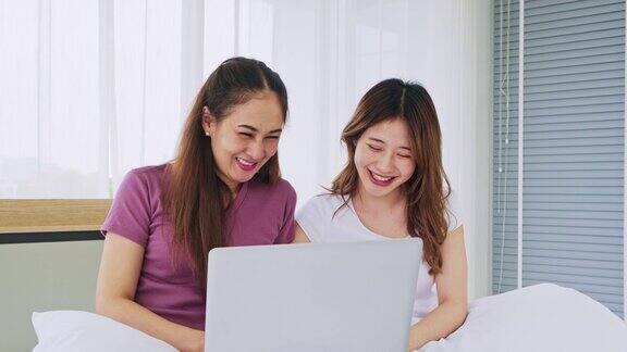 幸福的亚洲女性夫妇早上躺在床上用笔记本电脑一起笑着网上购物女性使用笔记本电脑进行社交、聊天或网上购物