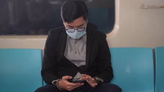 担心的亚洲商人戴着外科口罩防止感染冠状病毒坐在地铁用智能手机2019冠状病毒病大流行期间公共交通保持社交距离成为新常态