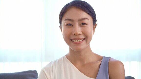 放大一个美丽的亚洲年轻女子穿着运动服坐在沙发上看着镜头微笑在她的脸在客厅