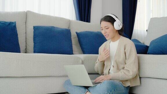 年轻的亚洲妇女戴着耳机在家里用笔记本电脑工作在家办公视频会议视频通话学生在线学习