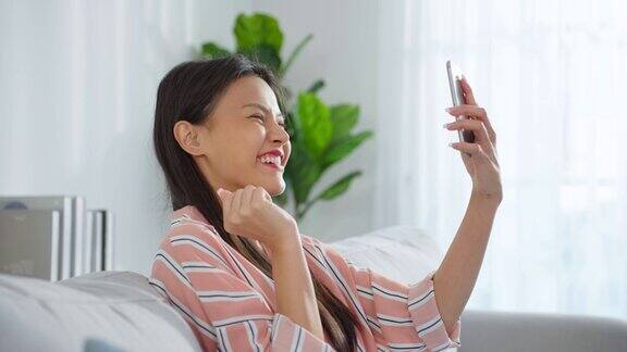亚洲美女使用手机视频通话在客厅年轻美丽的女孩感觉快乐和放松享受网上聊天虚拟电话在智能手机在家里科技生活方式