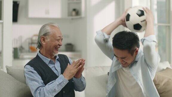 亚洲老年父亲和成年儿子喜欢在家里看电视上的足球比赛