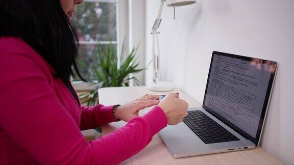 一名妇女在家用笔记本电脑工作时用脉搏血氧计测量心率