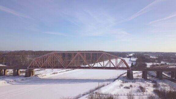 悬索式铁路桥用于冬季冰冻河上的火车交通景观鸟瞰图汽车交通在冬季高速公路上的火车桥无人机视图