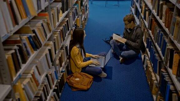 SLOMO学生在图书馆书架之间的地板上一起学习