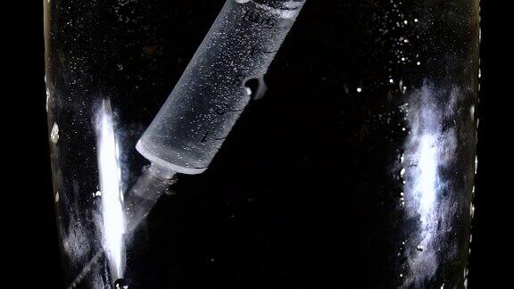 一个注射器漂浮在一杯水中的特写慢镜头拍摄