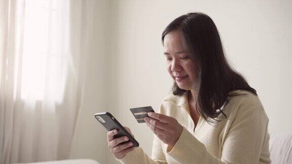 坐在床上的女人用信用卡和智能手机在网上付款