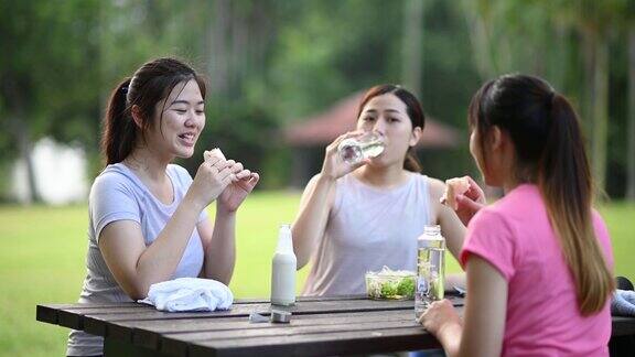 3个亚洲中国年轻女子在公园休息后早上锻炼吃健康的食物和饮料在公园长椅