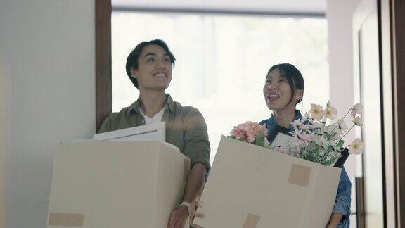 幸福的年轻亚洲夫妇拿着储物箱搬进新家
