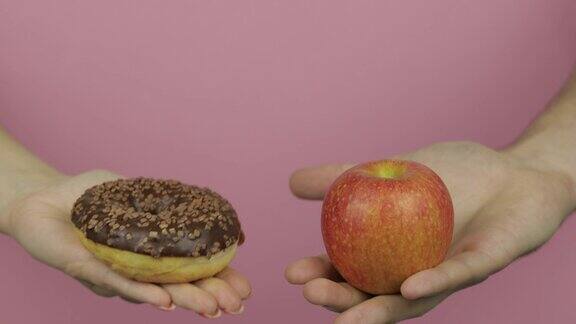 手里拿着甜甜圈和苹果选择甜甜圈而不是苹果健康或垃圾食品